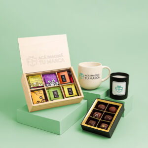 Set de infusiones premium con taza, vela negra y caja de bombones sobre pedestal verde claro.