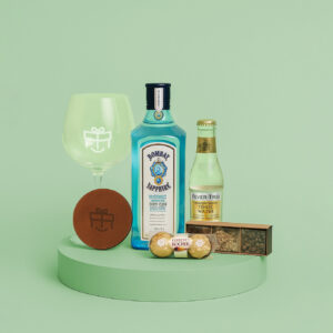 Set premium con gin Bombay, copón, tónica, especias, bombones y posavaso sobre pedestal verde claro.