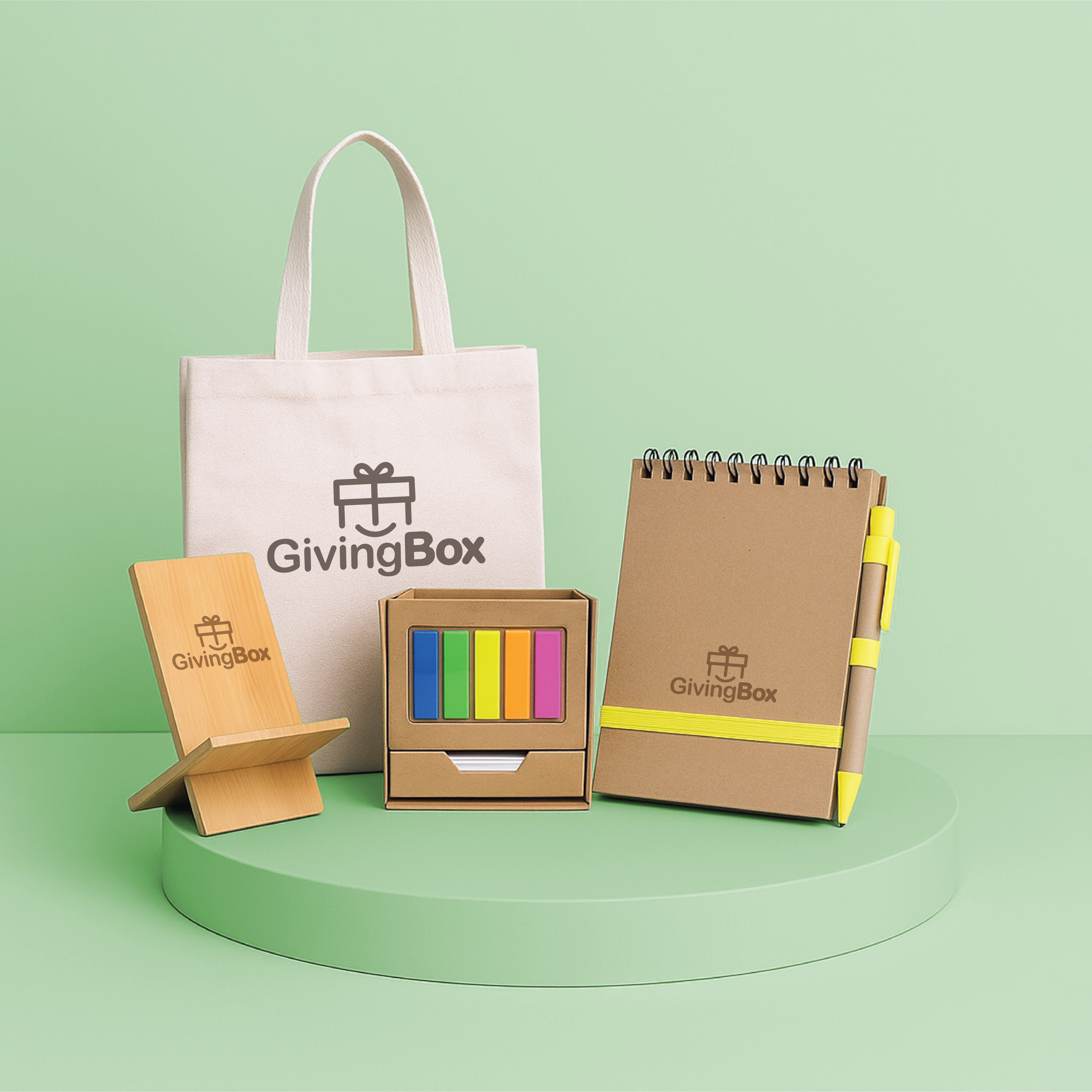 Kit de oficina ecológico con soporte para celular, cuaderno reciclado, porta lápices con post-it, y tote bag sobre pedestal verde.