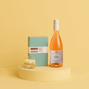 Kit con vino rosado Santa Julia, caja de chocolates Rapanui cerrada y vela aromática sobre pedestal amarillo.
